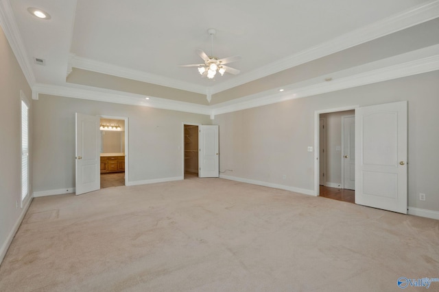 unfurnished bedroom with light carpet, baseboards, ensuite bath, ornamental molding, and a tray ceiling