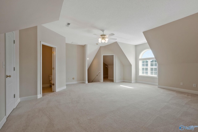 additional living space with light colored carpet, a ceiling fan, vaulted ceiling, a textured ceiling, and baseboards