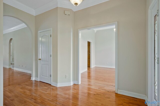 interior space featuring arched walkways, light wood finished floors, baseboards, and crown molding