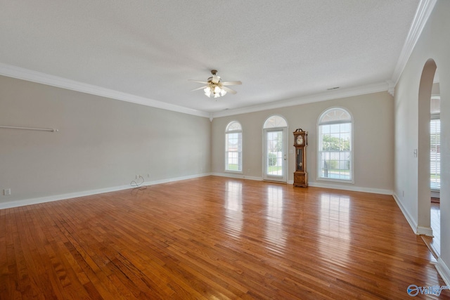 unfurnished living room with baseboards, arched walkways, a ceiling fan, wood-type flooring, and ornamental molding