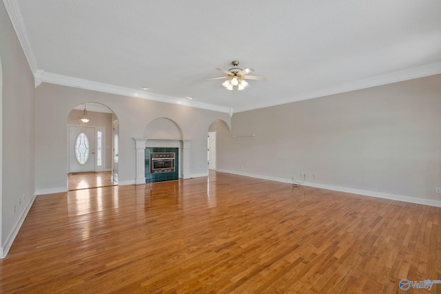 unfurnished living room featuring arched walkways, light wood finished floors, ornamental molding, and baseboards