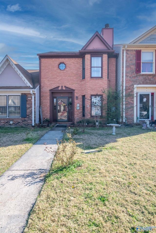 view of front facade featuring brick siding, a chimney, and a front lawn