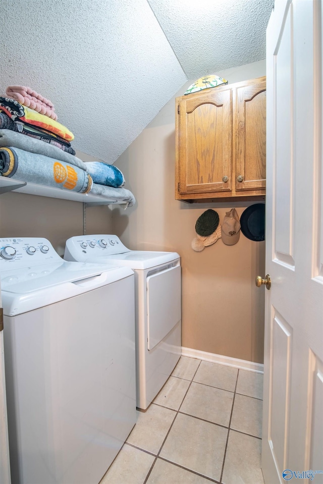 laundry room featuring baseboards, washing machine and dryer, light tile patterned floors, cabinet space, and a textured ceiling