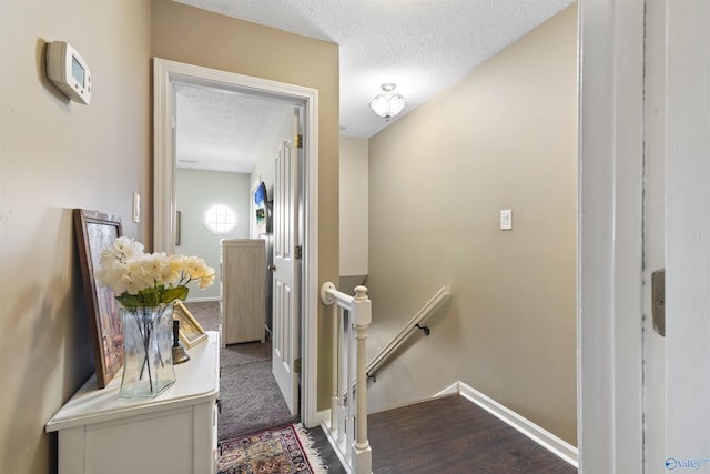 hall featuring an upstairs landing, a textured ceiling, baseboards, and wood finished floors