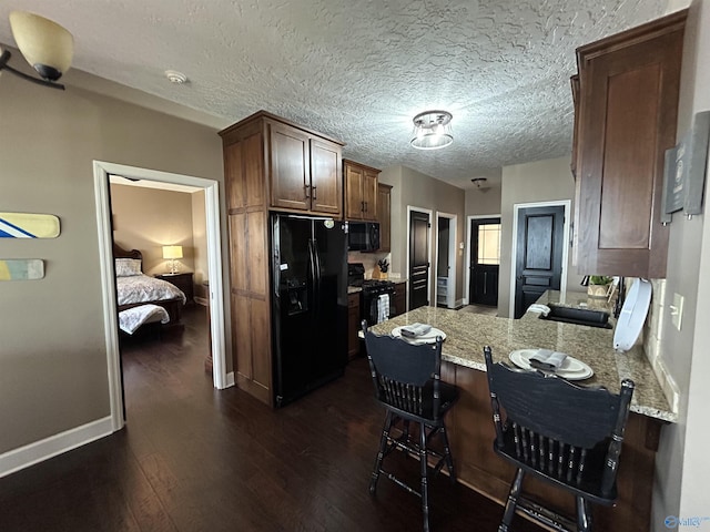 kitchen featuring dark wood-type flooring, a peninsula, light stone countertops, black appliances, and a sink