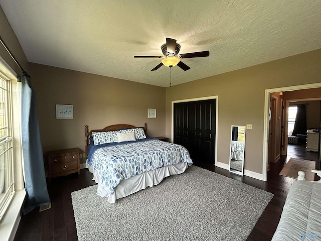 bedroom with a textured ceiling, dark wood-type flooring, a closet, and baseboards