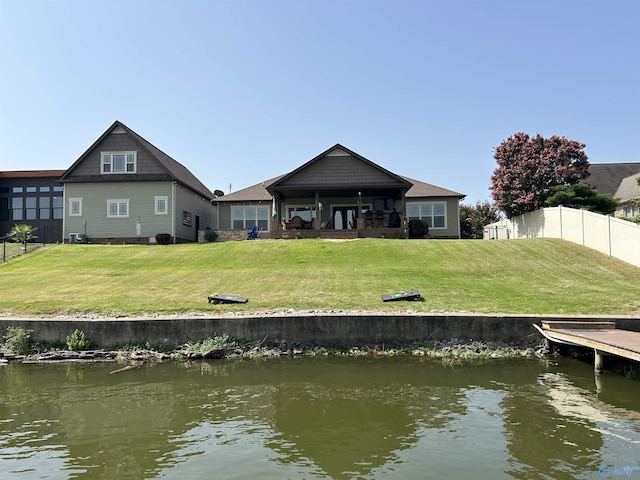 back of property with a water view, fence, and a lawn