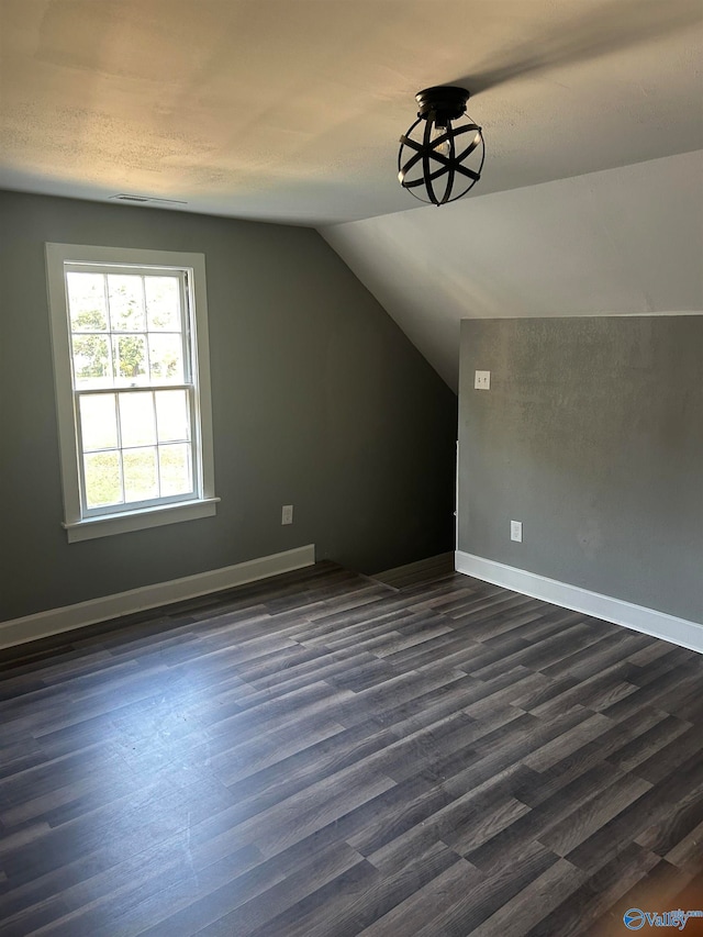 additional living space featuring dark hardwood / wood-style floors, a textured ceiling, and vaulted ceiling