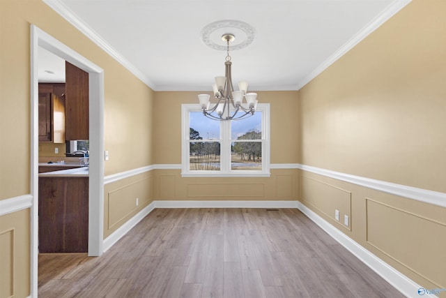 unfurnished dining area with ornamental molding, a chandelier, and light hardwood / wood-style floors