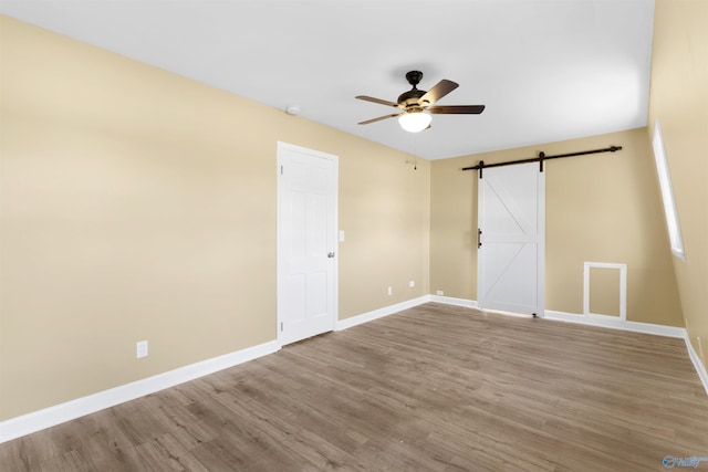 unfurnished room with light hardwood / wood-style floors, ceiling fan, and a barn door