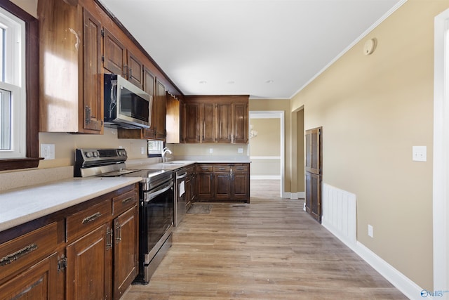 kitchen with light wood-type flooring, appliances with stainless steel finishes, ornamental molding, and sink