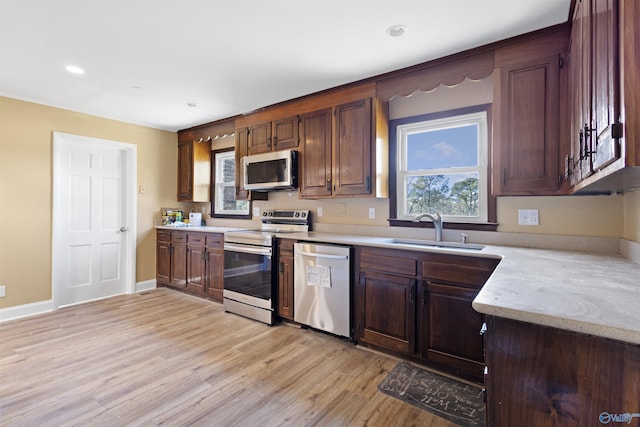 kitchen with appliances with stainless steel finishes, sink, light stone counters, and light hardwood / wood-style flooring