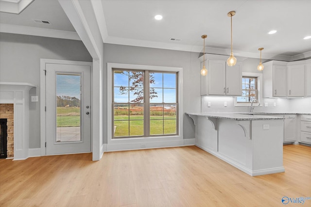 kitchen with a fireplace, white cabinets, light stone countertops, a breakfast bar, and light hardwood / wood-style flooring