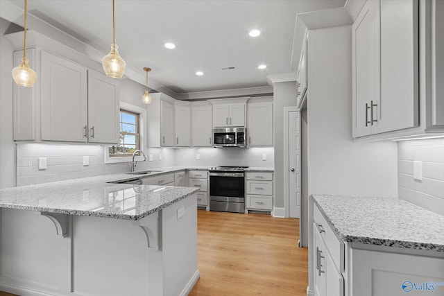 kitchen featuring light hardwood / wood-style flooring, stainless steel appliances, decorative light fixtures, decorative backsplash, and light stone countertops