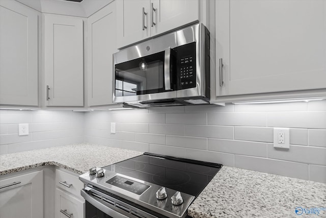 kitchen featuring appliances with stainless steel finishes, light stone counters, backsplash, and white cabinetry