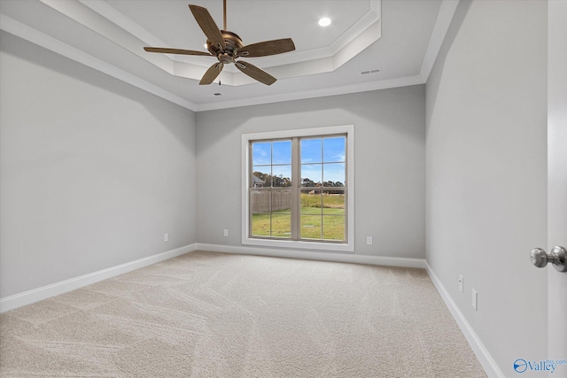 empty room with crown molding, a raised ceiling, light colored carpet, and ceiling fan