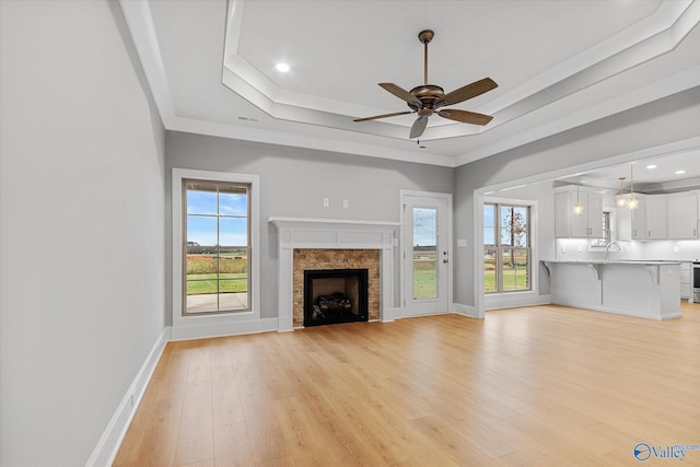 unfurnished living room with light hardwood / wood-style flooring, ceiling fan, a raised ceiling, a tile fireplace, and sink