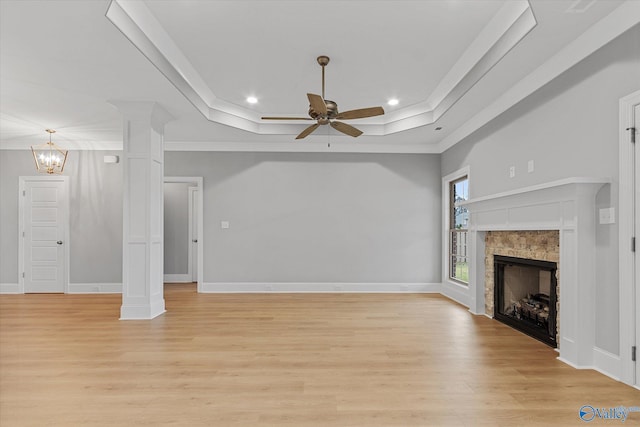 unfurnished living room featuring a tray ceiling, ceiling fan with notable chandelier, ornamental molding, ornate columns, and light hardwood / wood-style flooring