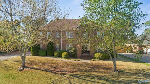 colonial inspired home featuring concrete driveway, brick siding, and a front lawn