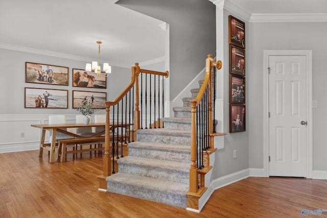 stairway with a chandelier, crown molding, wood finished floors, and baseboards