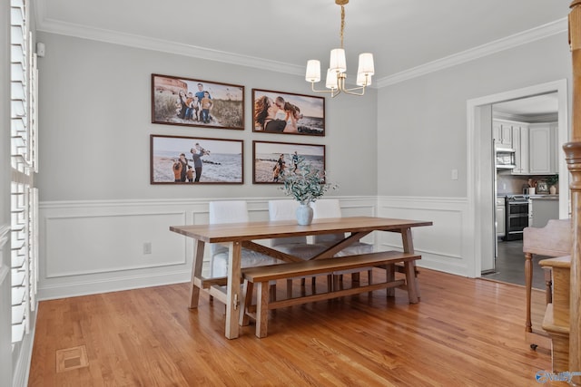 dining space featuring light wood-style flooring, ornamental molding, visible vents, wainscoting, and a notable chandelier