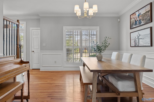 dining room featuring an inviting chandelier, a decorative wall, light wood-type flooring, crown molding, and a wainscoted wall