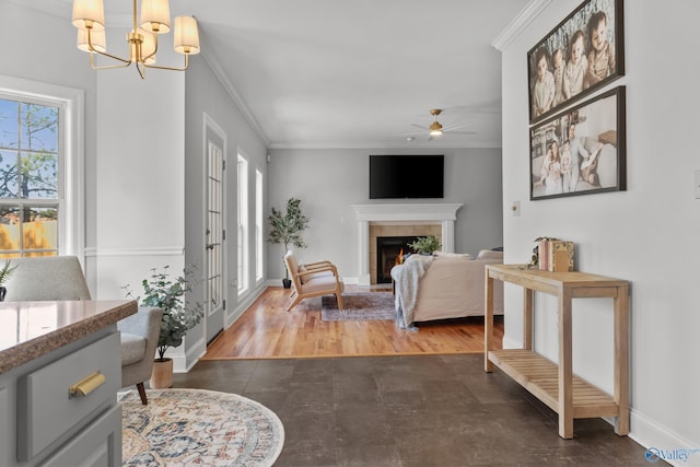 living room featuring baseboards, a tiled fireplace, ceiling fan with notable chandelier, and crown molding