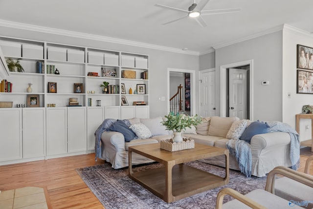 living area featuring crown molding, light wood finished floors, a ceiling fan, and stairs