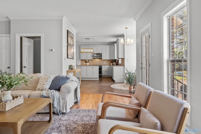 living area with ornamental molding, light wood finished floors, and an inviting chandelier