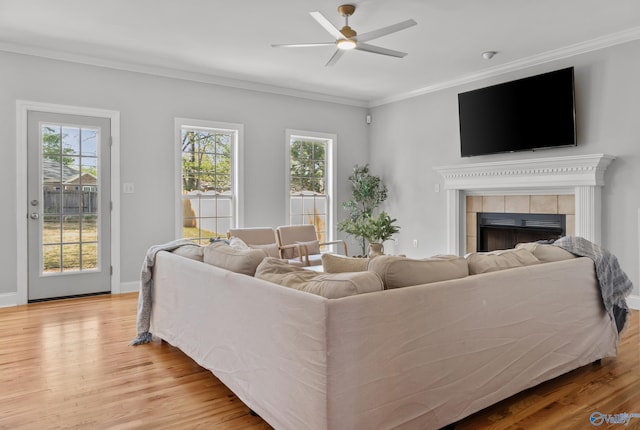 living area featuring crown molding, wood finished floors, a healthy amount of sunlight, a tile fireplace, and ceiling fan