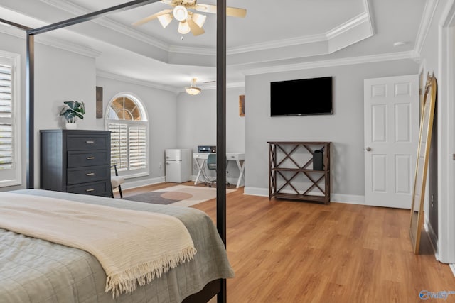 bedroom featuring baseboards, freestanding refrigerator, crown molding, a tray ceiling, and light wood finished floors