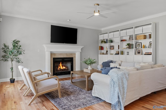 living area with wood finished floors, ceiling fan, a fireplace, and ornamental molding