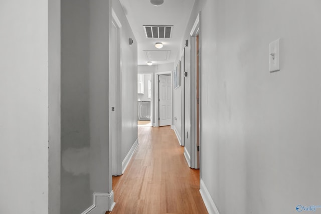 corridor with light wood-style floors, attic access, baseboards, and visible vents