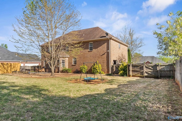 back of property featuring a yard, a fenced backyard, brick siding, and a gate