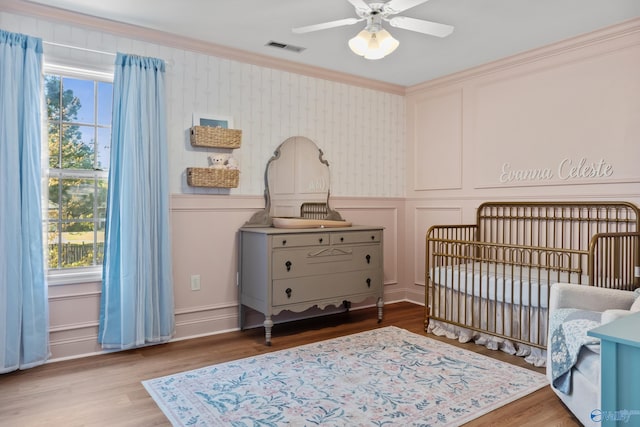 bedroom with a decorative wall, wood finished floors, ornamental molding, and visible vents