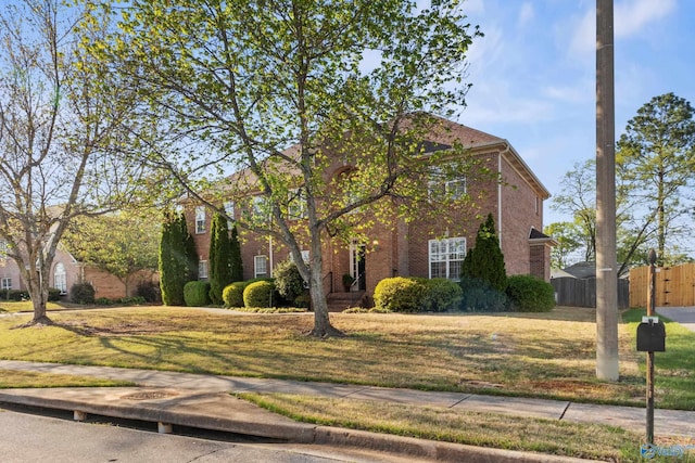 view of front facade featuring brick siding, a front lawn, and fence