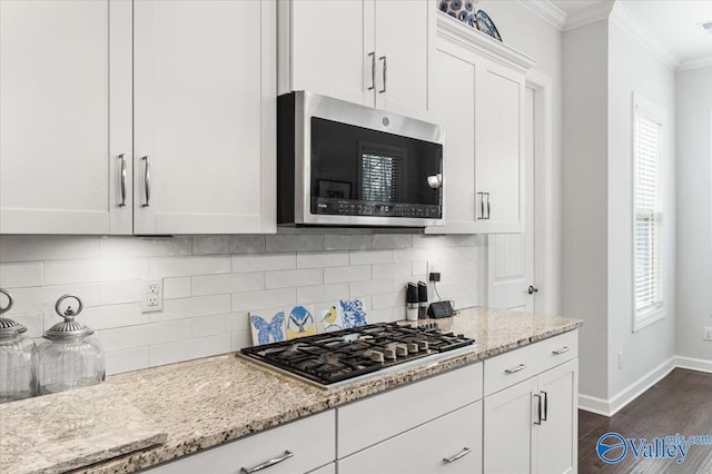 kitchen featuring dark wood finished floors, crown molding, decorative backsplash, appliances with stainless steel finishes, and light stone countertops