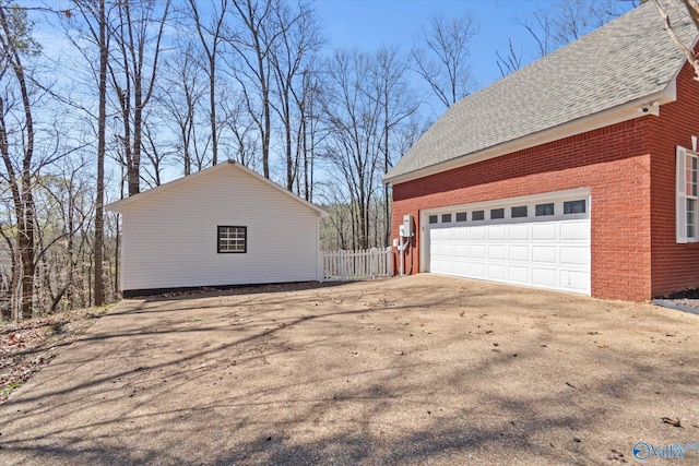 view of property exterior with fence, a garage, brick siding, driveway, and a shingled roof