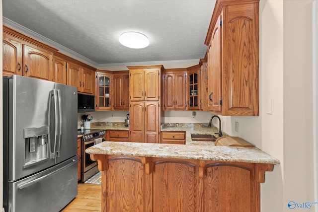 kitchen featuring a sink, a peninsula, brown cabinets, glass insert cabinets, and stainless steel appliances