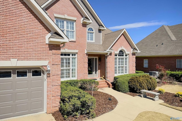 traditional-style house featuring a garage, brick siding, a shingled roof, and central AC