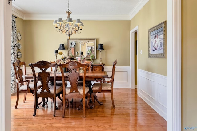 dining room with a chandelier, a wainscoted wall, light wood-type flooring, and crown molding