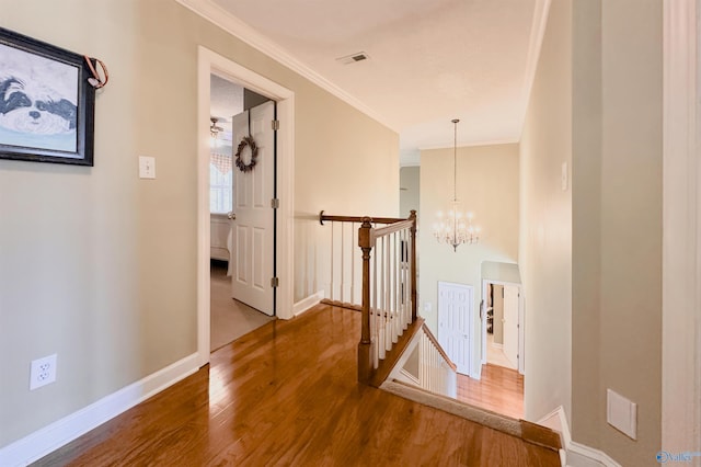 hall featuring visible vents, ornamental molding, wood finished floors, an upstairs landing, and a notable chandelier