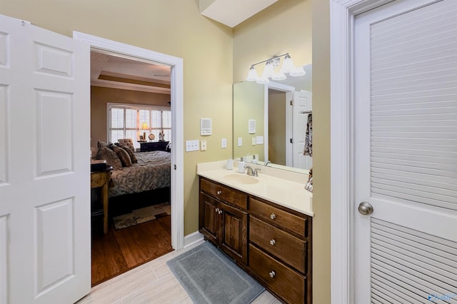 ensuite bathroom with ensuite bath, baseboards, wood finished floors, and vanity