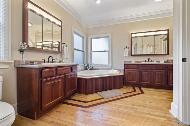 bathroom with toilet, hardwood / wood-style floors, ornamental molding, a washtub, and vanity