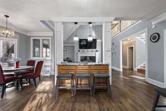 kitchen featuring a textured ceiling, dark wood-type flooring, hanging light fixtures, kitchen peninsula, and light stone counters