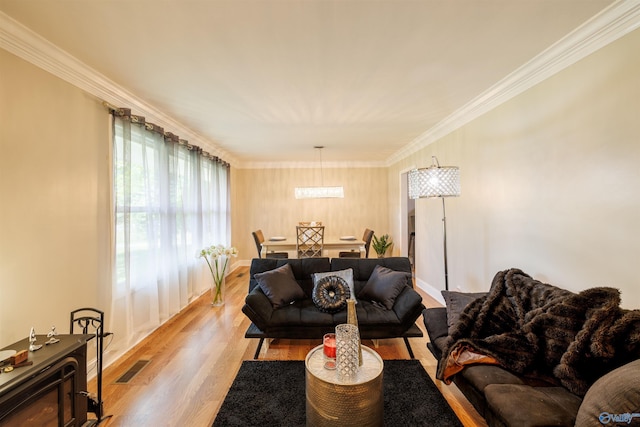 living area with ornamental molding, light wood-type flooring, and visible vents