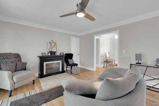 living area with a fireplace, a ceiling fan, baseboards, light wood-style floors, and ornamental molding