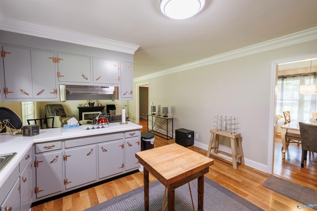 kitchen featuring crown molding, white stovetop, light countertops, light wood-type flooring, and baseboards