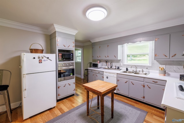 kitchen featuring white appliances, ornamental molding, light countertops, light wood-style floors, and a sink