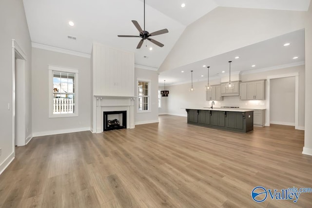 unfurnished living room featuring sink, light hardwood / wood-style flooring, ceiling fan, high vaulted ceiling, and ornamental molding